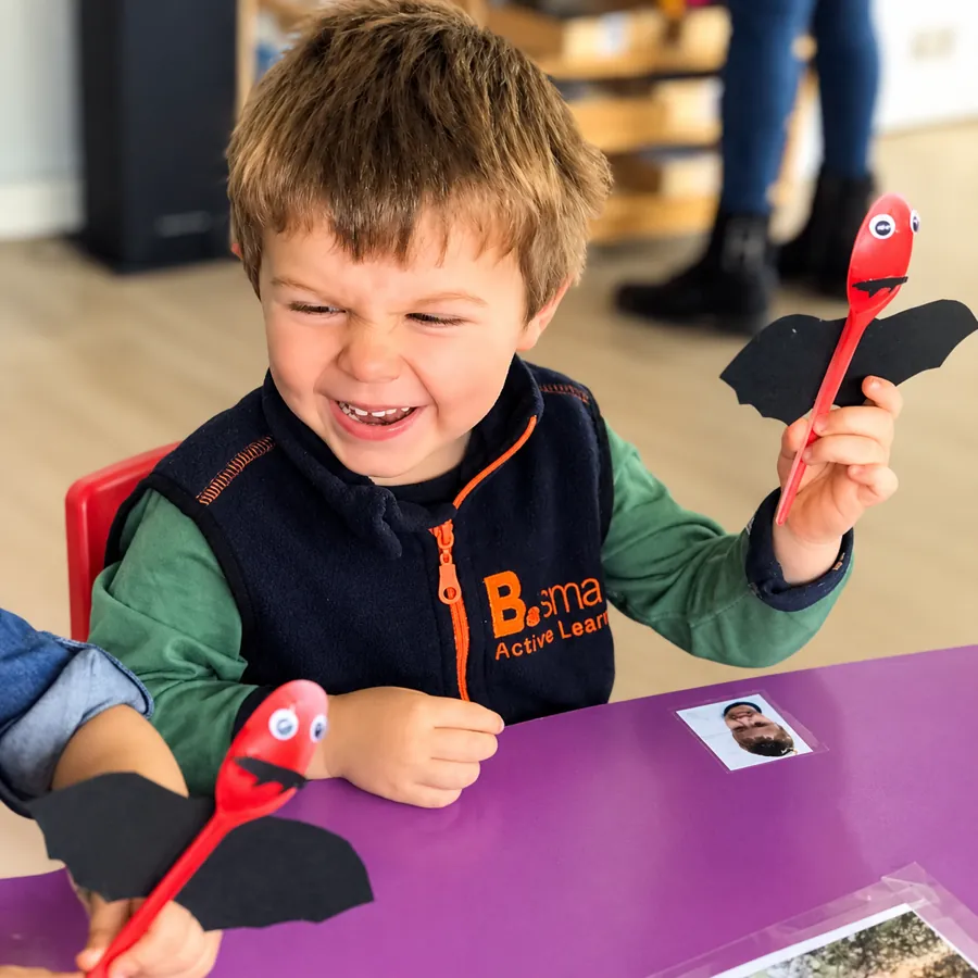 Enfant riant avec sa chauve-souris en cuillère fabriquée en atelier bricolage à la crèche B.smart