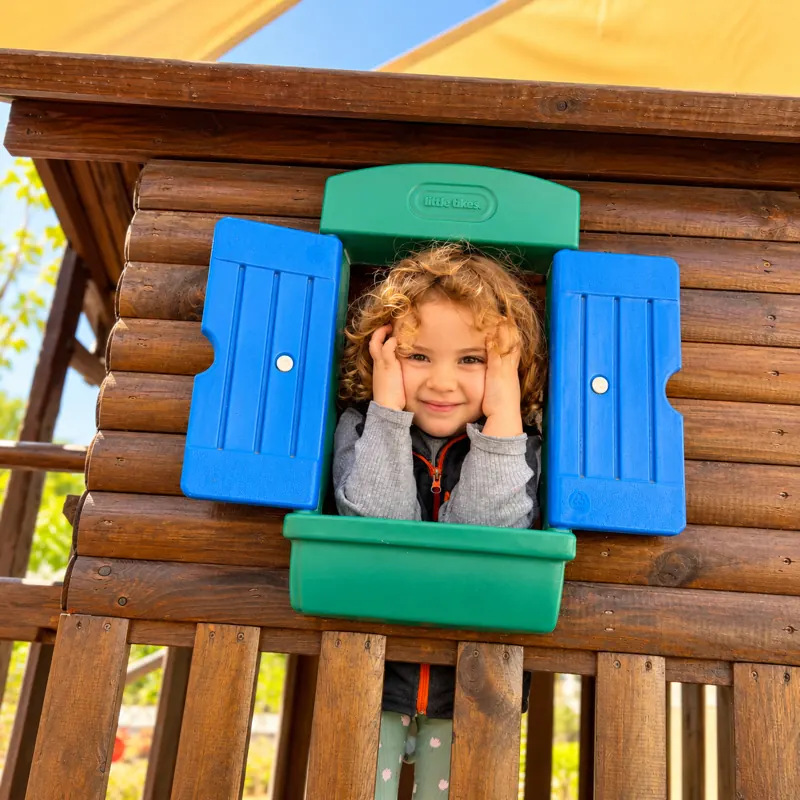 Fillette souriante à la fenêtre de la cabane du jardin de la crèche B.smart