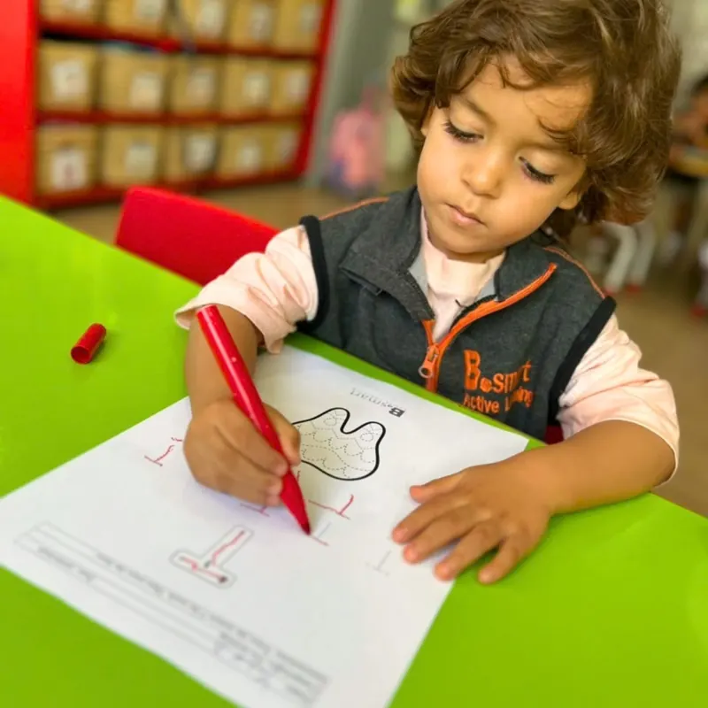Enfant traçant des lettres au feutre rouge en classe à la crèche B.smart