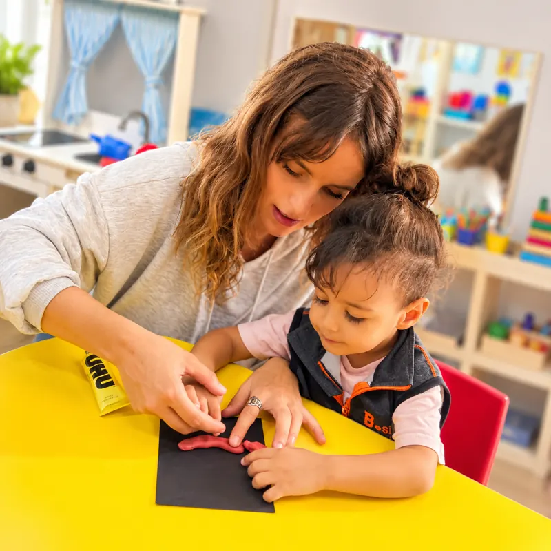 Éducatrice aidant un tout-petit à modeler de la pâte à la crèche B.smart