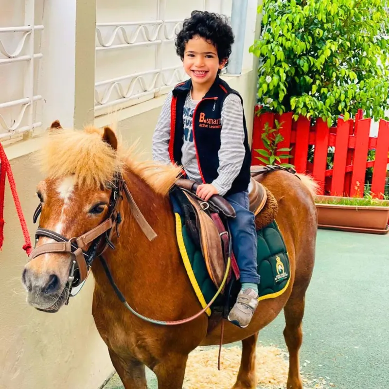 Enfant souriant sur un poney lors de la journée poney à la crèche B.smart