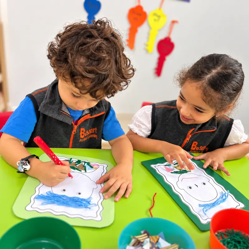 Deux enfants décorant leur autoportrait en atelier collage à la crèche B.smart
