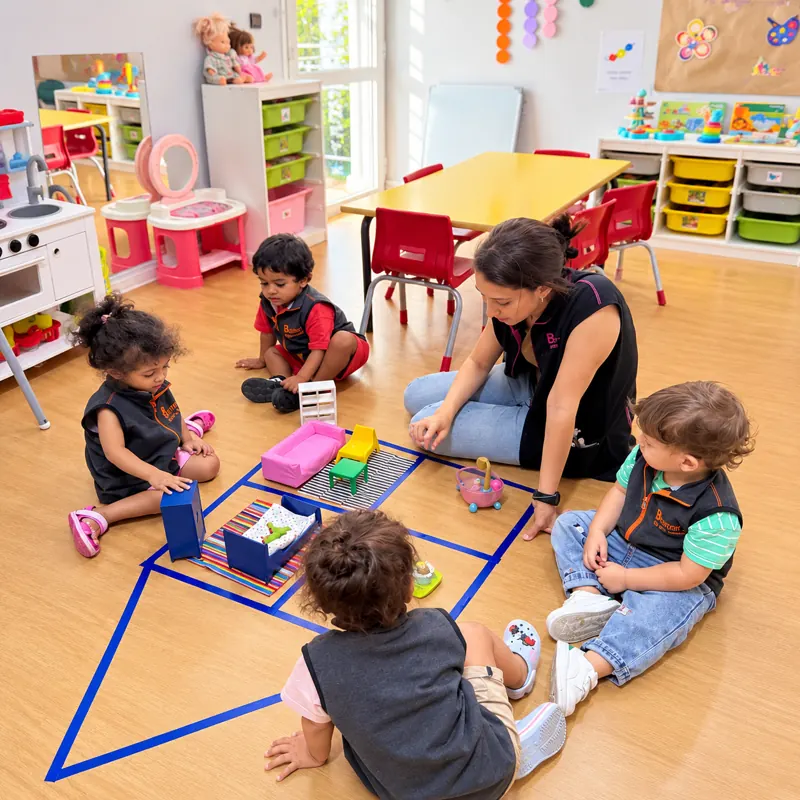 Tout-petits jouant à la maison de poupée avec leur éducatrice dans la classe Toddlers