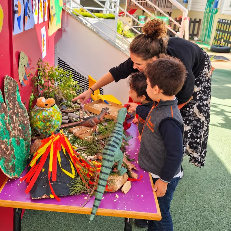 Enfants découvrant une maquette de volcan et de dinosaures avec leur éducatrice
