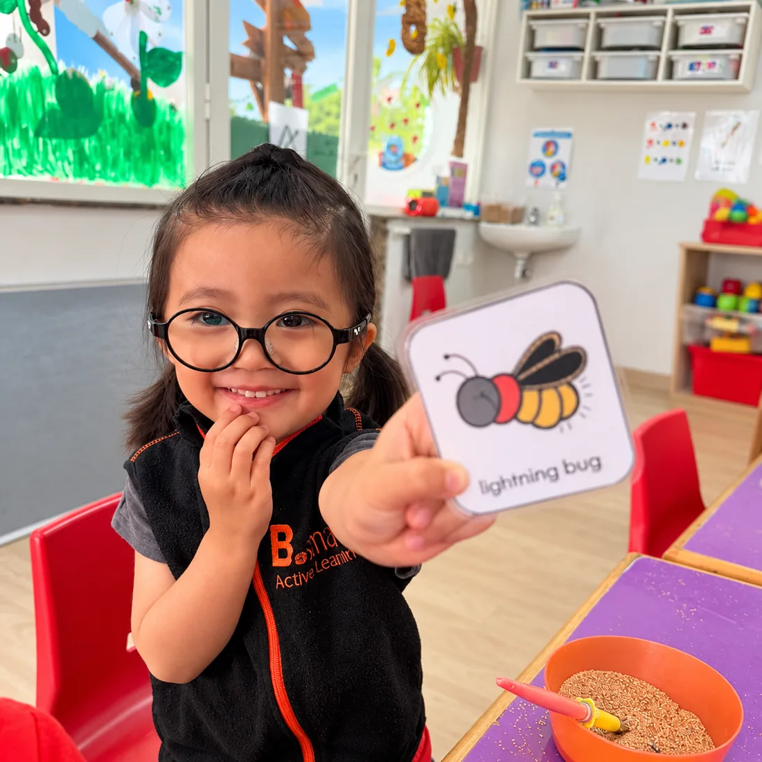 Fillette souriante montrant une carte de vocabulaire en anglais dans une classe de la crèche B.smart à Rabat