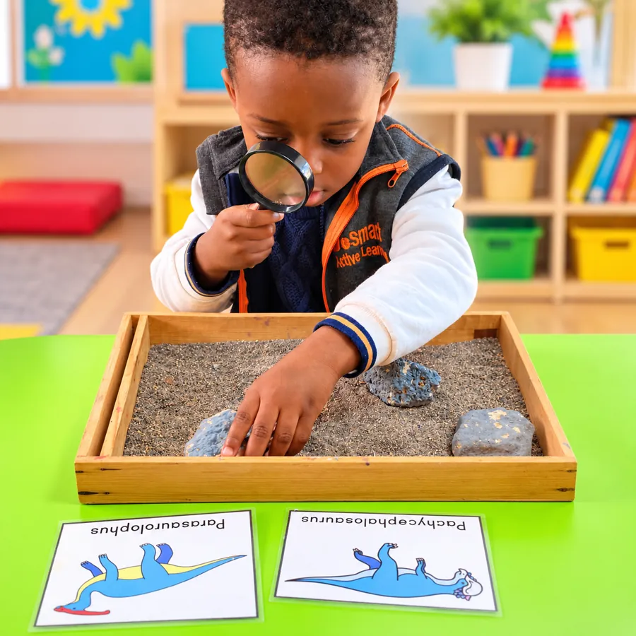Enfant observant à la loupe une fouille de dinosaures en classe à la crèche B.smart